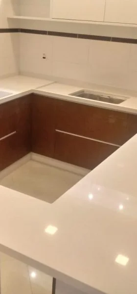 Cozinha em L com bancada branca e cuba embutida